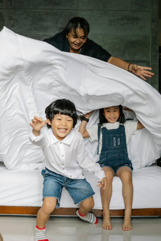 Photo d'une famille libre aves les enfants qui jouent à se cacher de la maman sous la couette du lit.